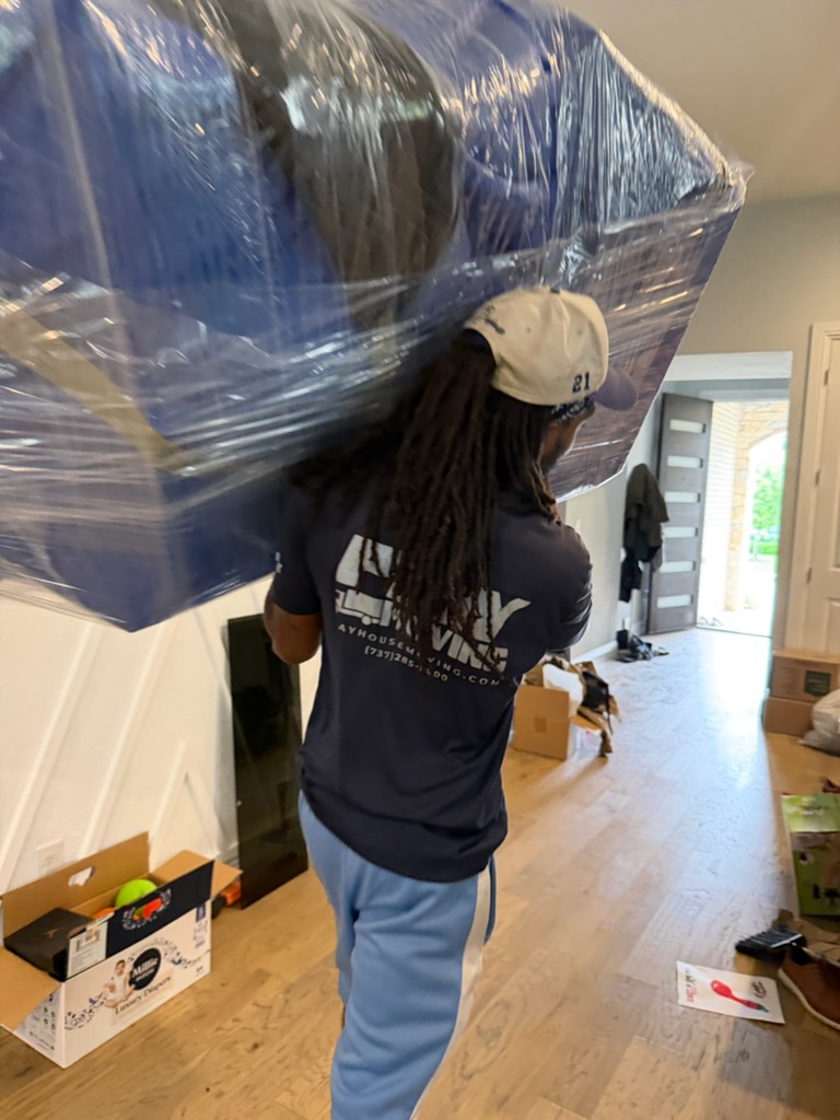 Playhouse Moving crew member carrying wrapped furniture inside a home